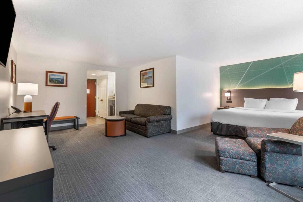 A hotel room with a bed, two armchairs, a desk, and a small table.