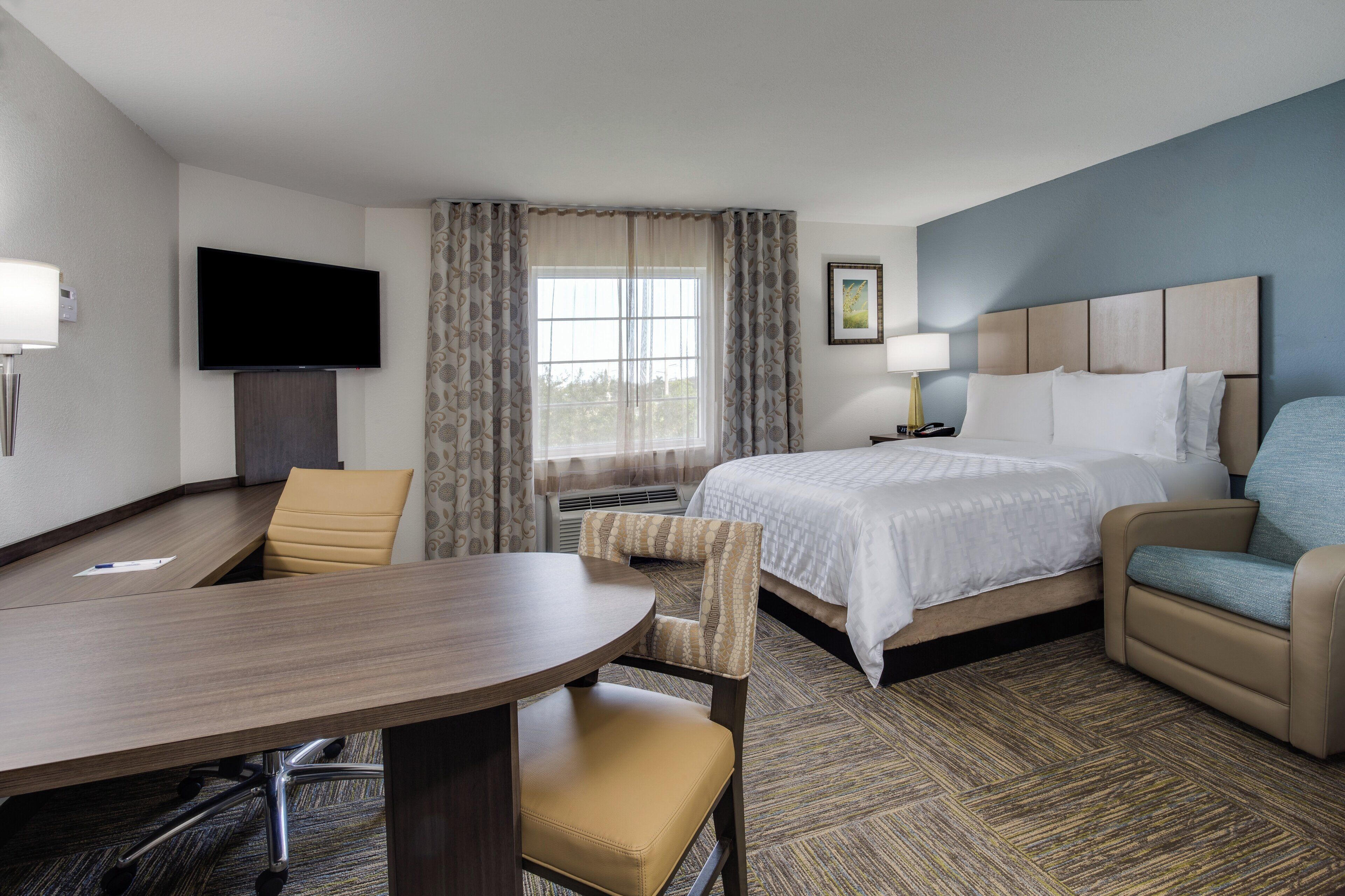 A hotel room with a bed, a desk, a chair, a television, and a window with curtains.