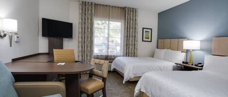 A hotel room with a desk, two beds, a TV, and a window with curtains.