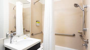 Une salle de bain équipée d’un lavabo, d’un miroir, d’une douche et de barres d’appui.