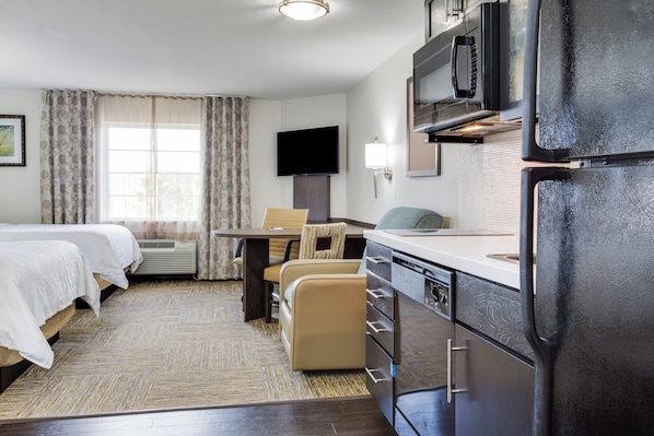 Habitación de hotel con cama, escritorio, silla, televisor y kitchenette.