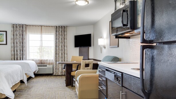 A hotel room with two beds, a dining table with chairs, a kitchen area with a refrigerator, and a TV mounted on the wall. - Candlewood Suites Ft. Lauderdale Airport/Cruise by IHG (Fort Lauderdale)