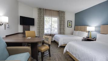 Een hotelkamer met een bed, bureau, stoel, televisie en raam met gordijnen.