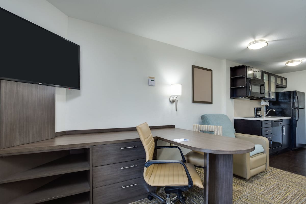 Une chambre d’hôtel moderne dotée d’un coin repas, d’une kitchenette et d’un téléviseur à écran plat fixé au mur.