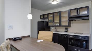 A modern kitchen with dark cabinets, a built-in oven, and a dining area with a wooden table and a single chair.