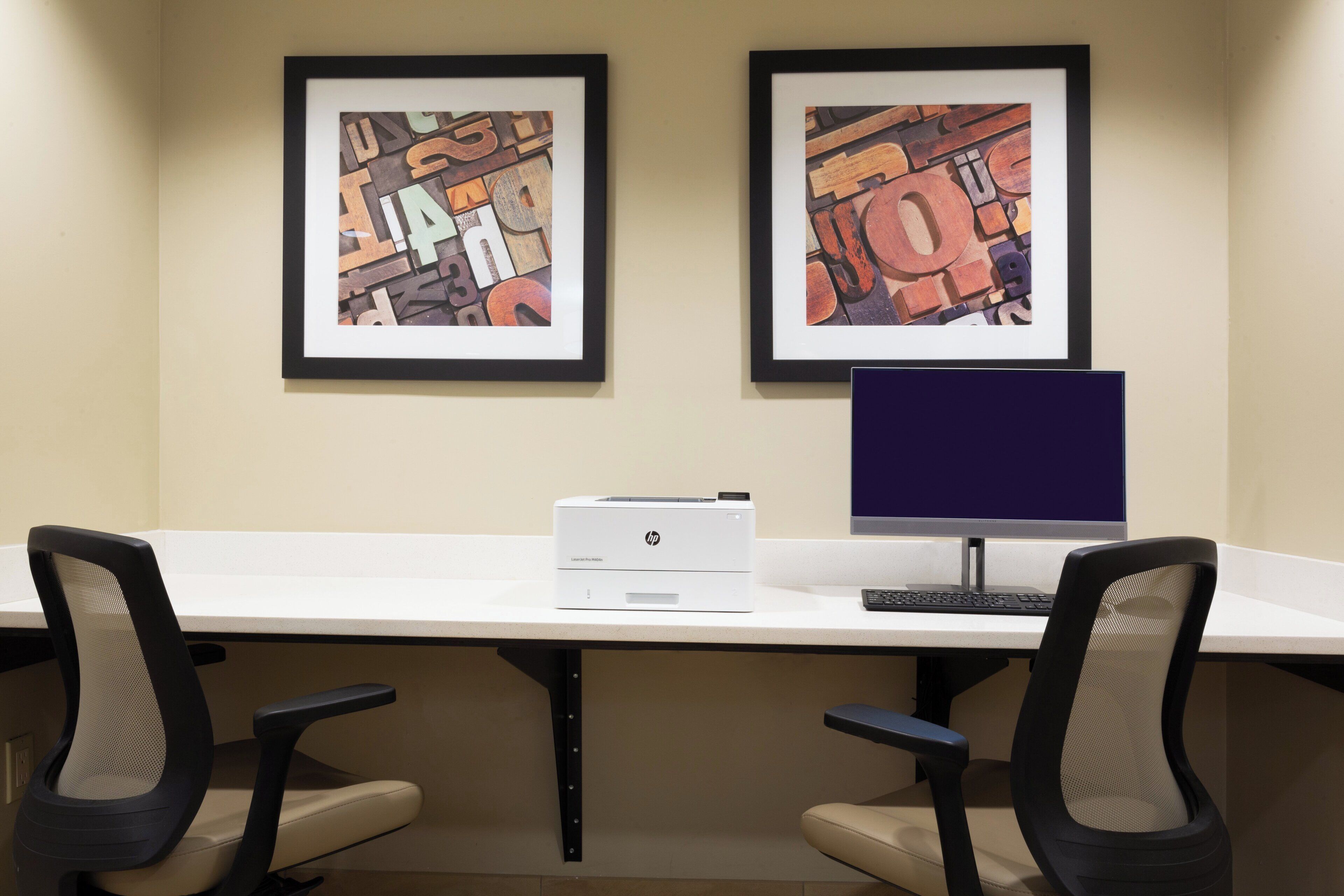 A workspace with two framed abstract artworks, a desktop computer, and office chairs.