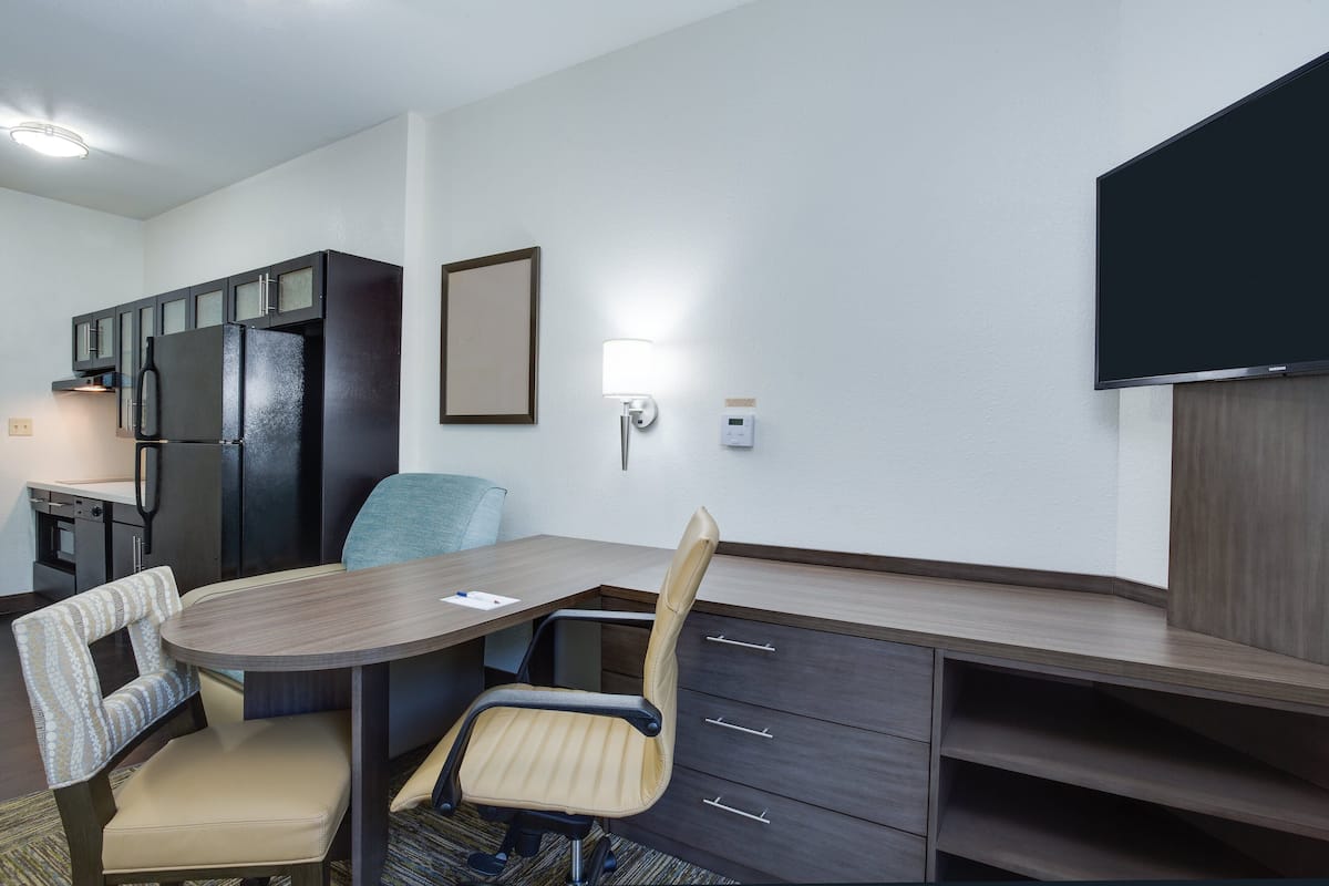 Une chambre d’hôtel compacte comprenant un coin cuisine, une table à manger avec deux chaises, un téléviseur à écran plat et un petit coin salon avec un fauteuil confortable.