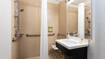 Un baño con ducha a nivel, barras de apoyo, lavamanos y espejo.