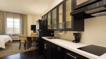 Uma cozinha de hotel compacta com área de jantar, geladeira, cafeteira e uma janela com cortinas.