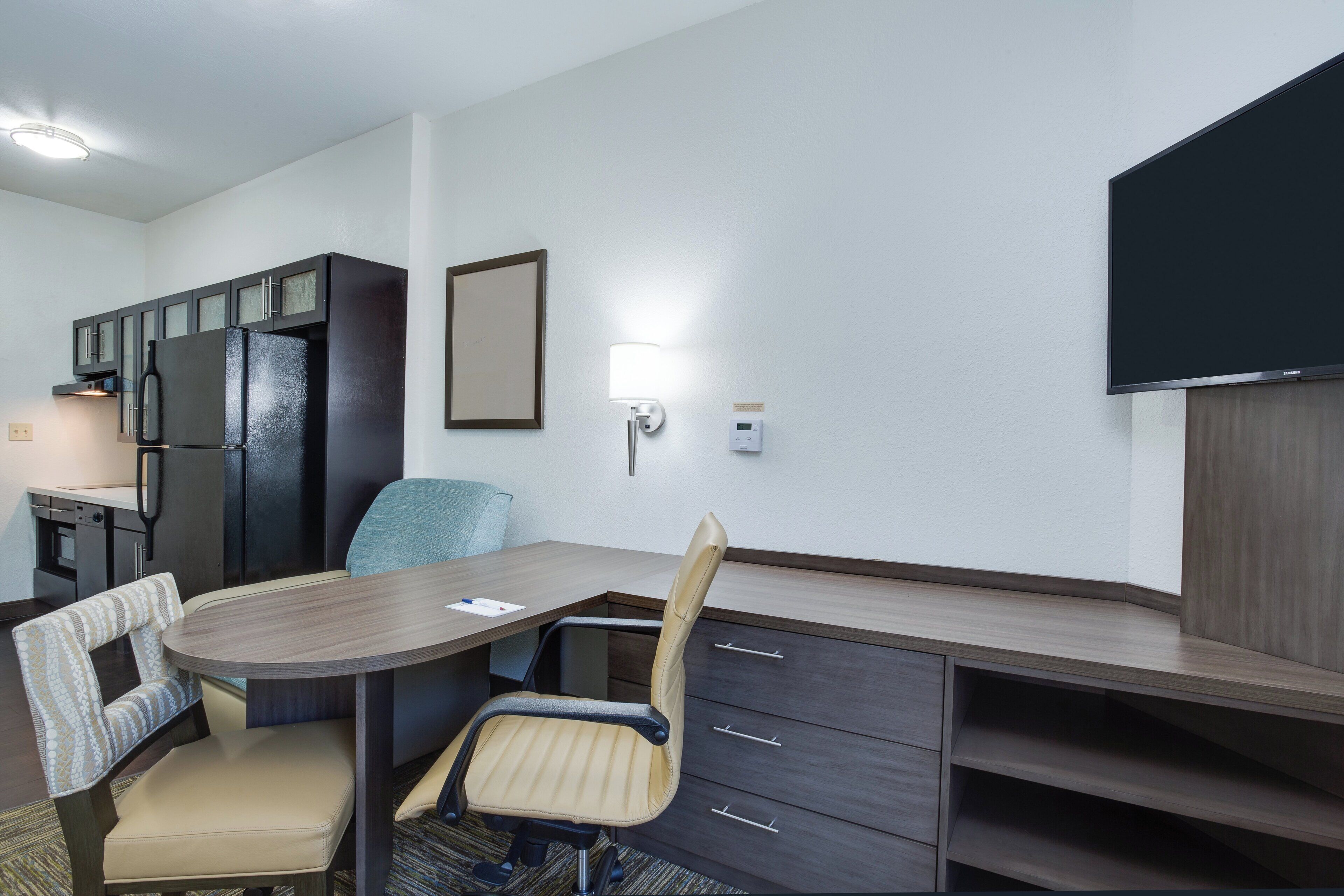 Ett kompakt hotellrum med ett litet pentry, ett matbord med två stolar, en soffa, en tv som är monterad på väggen och ett litet sidobord.