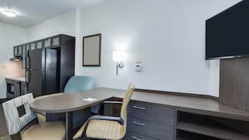 Ett kompakt hotellrum med ett litet pentry, ett matbord med två stolar, en soffa, en tv som är monterad på väggen och ett litet sidobord.