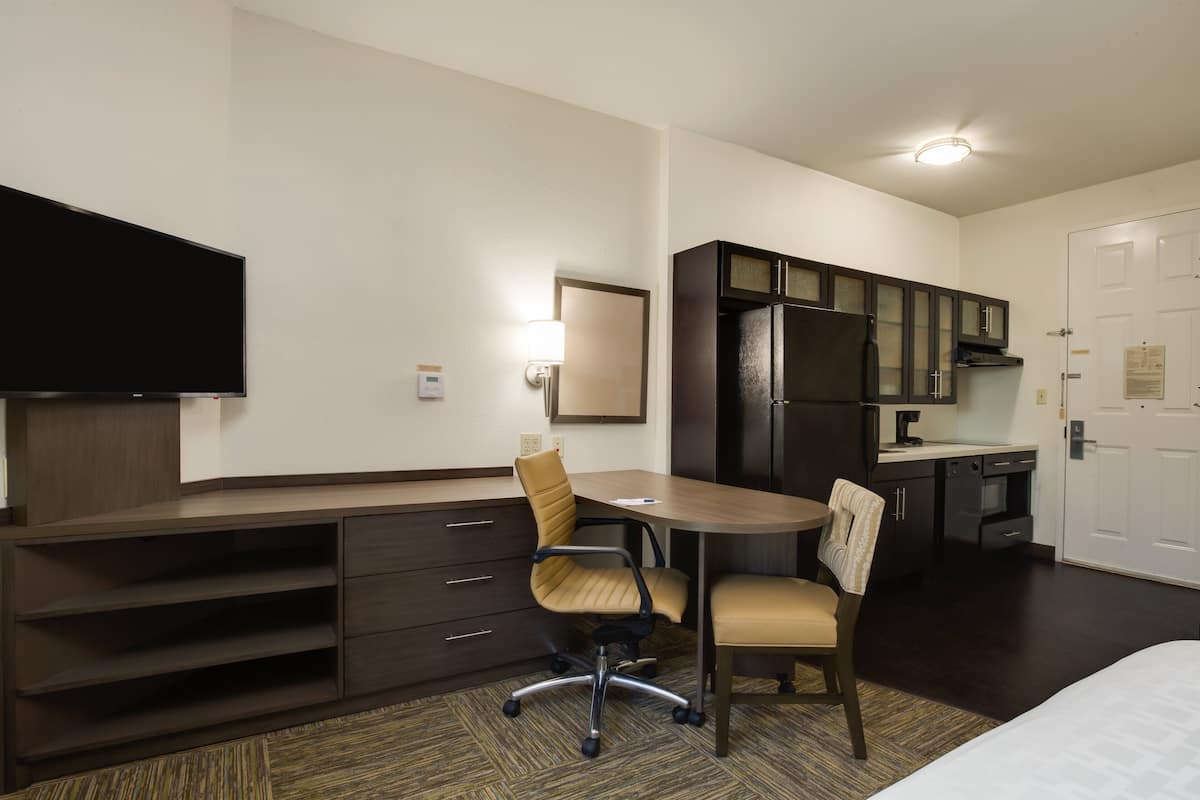 Une chambre d’hôtel équipée d’un bureau, de deux chaises, d’une télévision à écran plat, d’un four à micro-ondes et d’un réfrigérateur.