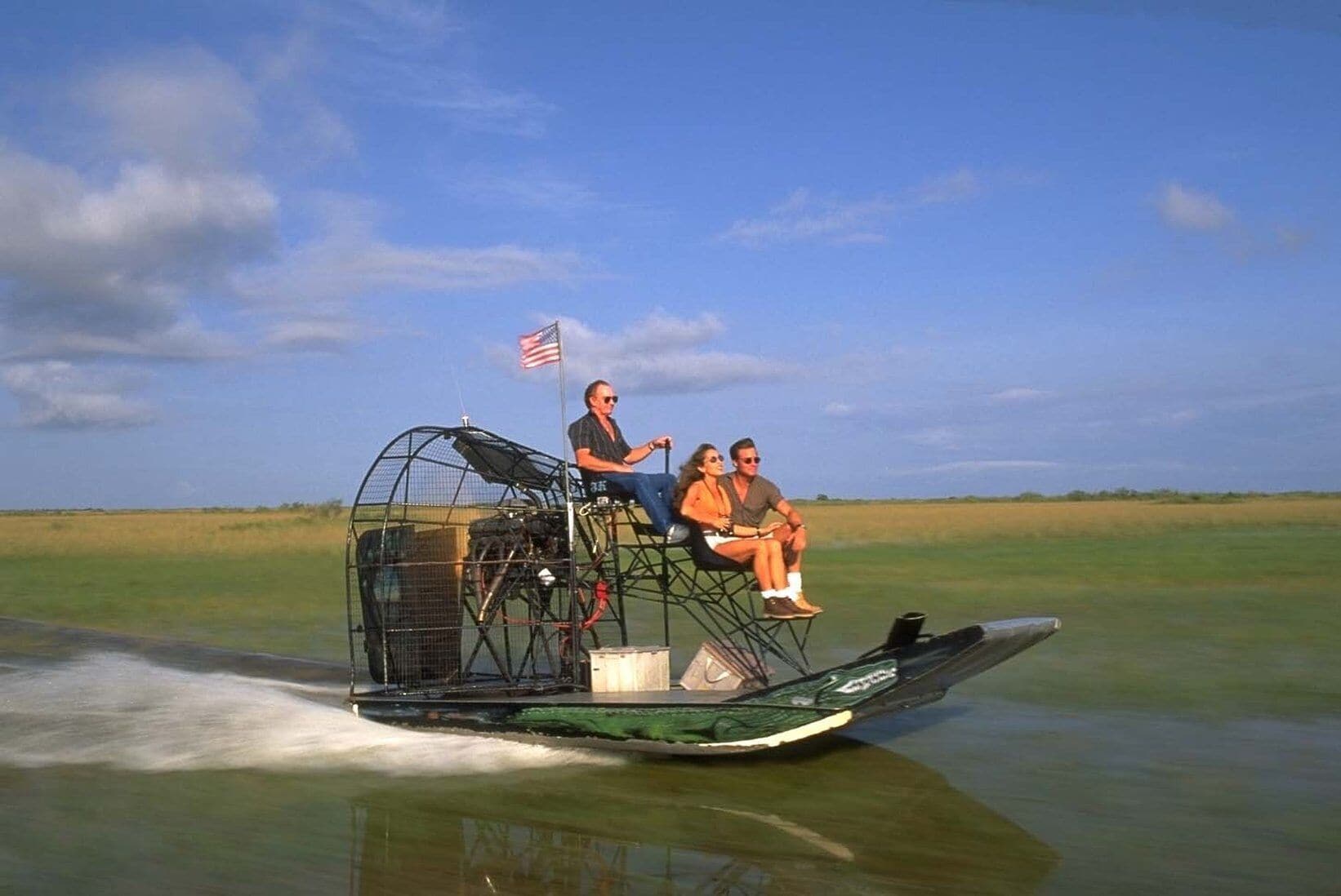 A watercraft with a cage-like structure on the back, passengers, and an American flag.
