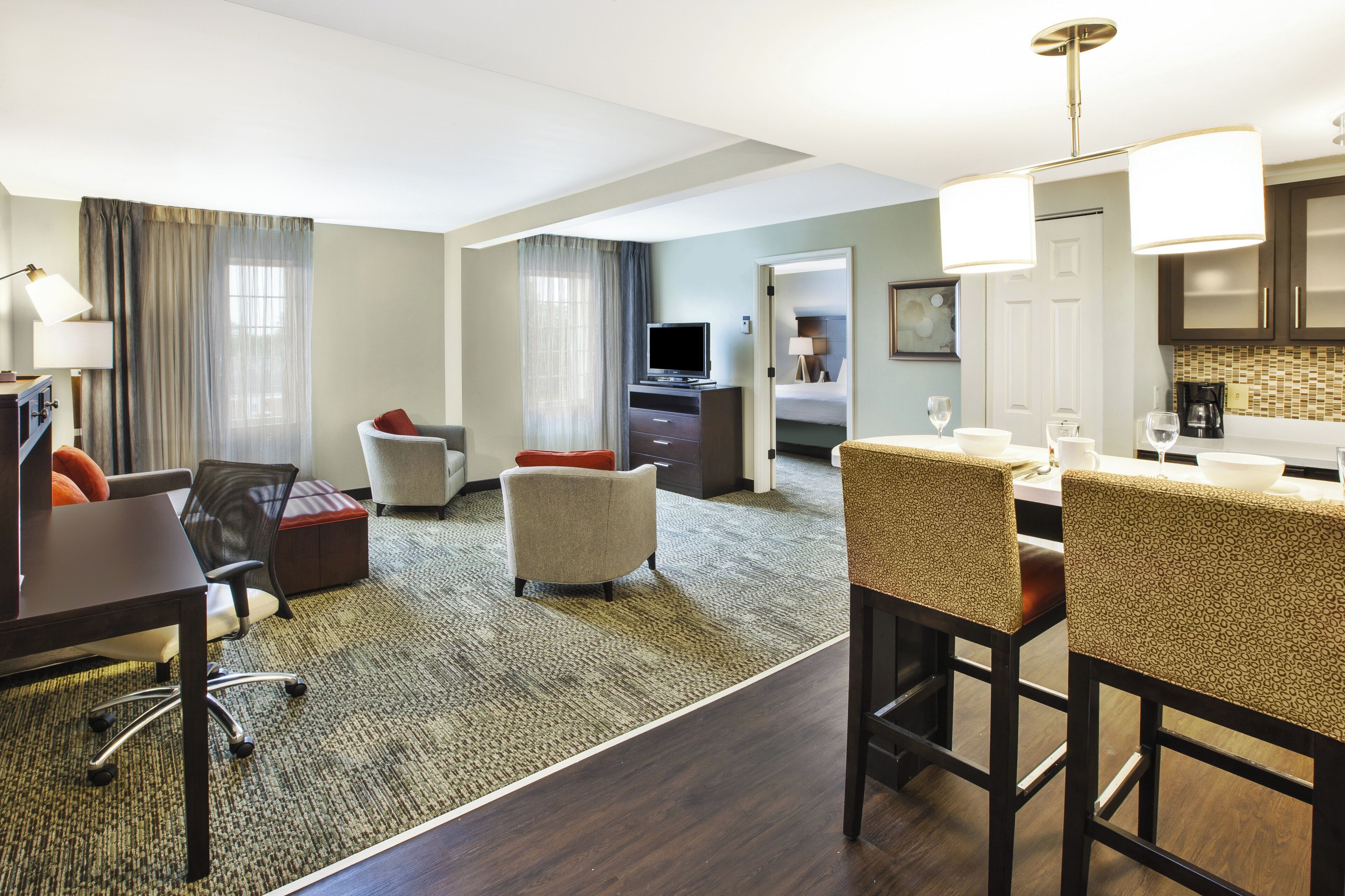 A hotel room with a living area, a dining space, a kitchenette, and a separate bedroom.