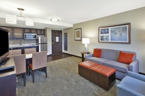 Een moderne hotelkamer met kitchenette, eethoek en een zithoek met bank en poef.