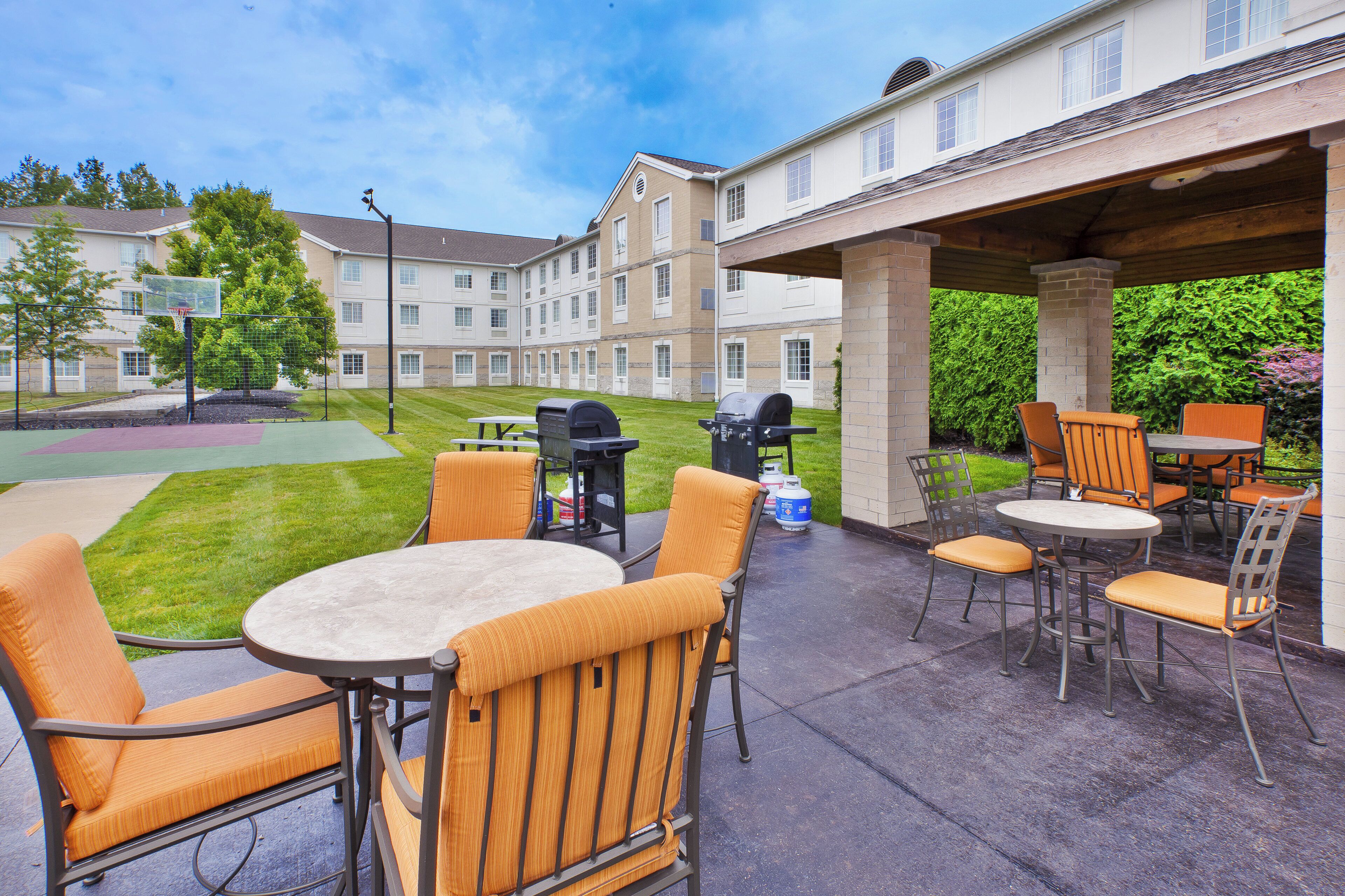 An outdoor patio area with tables and chairs, a barbecue grill, and a basketball court.