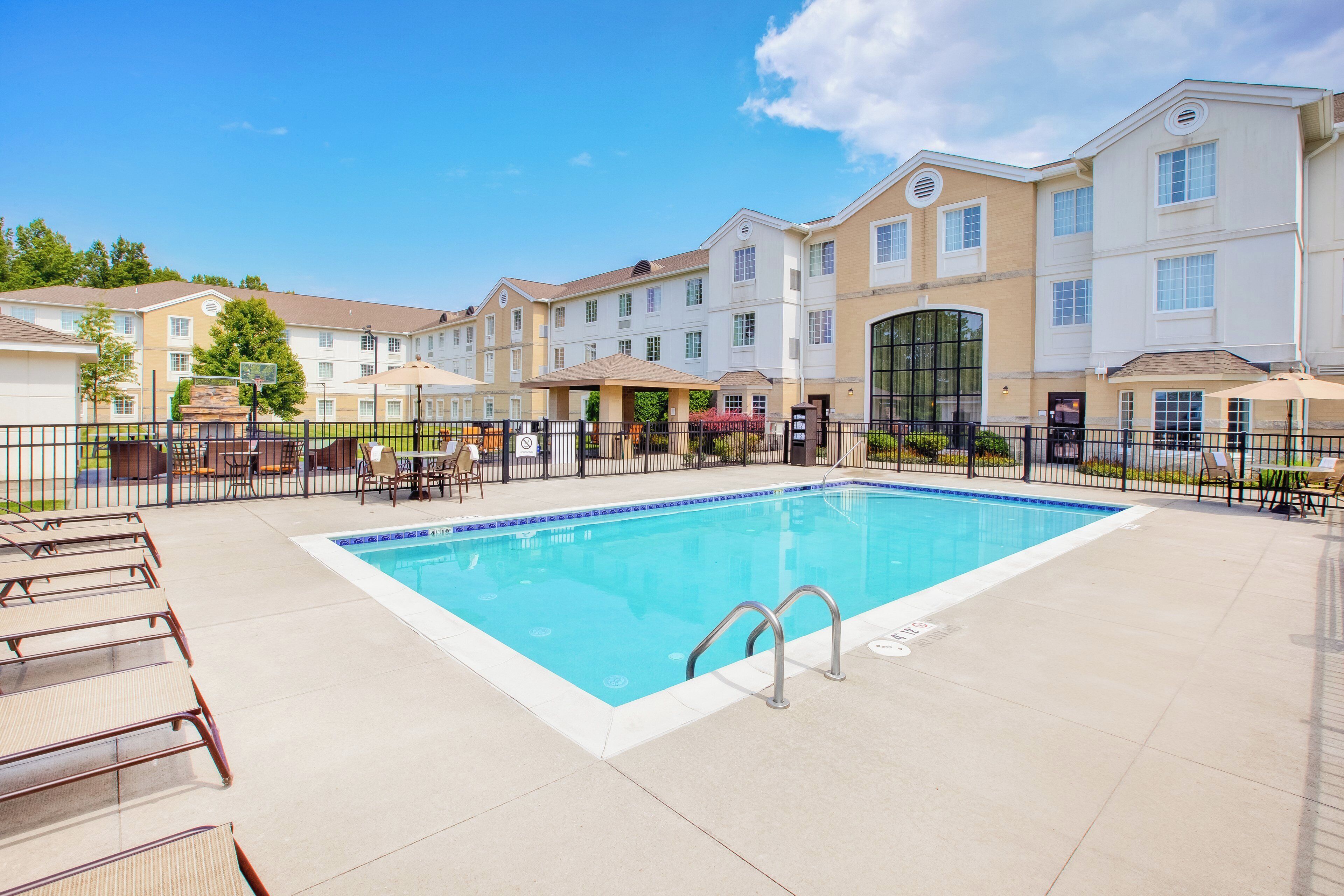 A rectangular pool with a tiled edge, surrounded by a fence, and adjacent to a row of multi-story buildings with balconies.