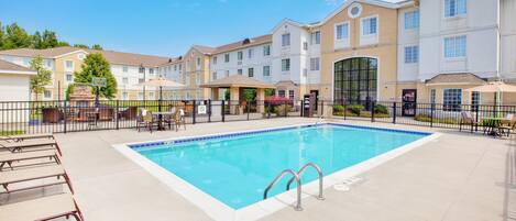 A rectangular pool with a tiled edge, surrounded by a fence, and adjacent to a row of multi-story buildings with balconies.