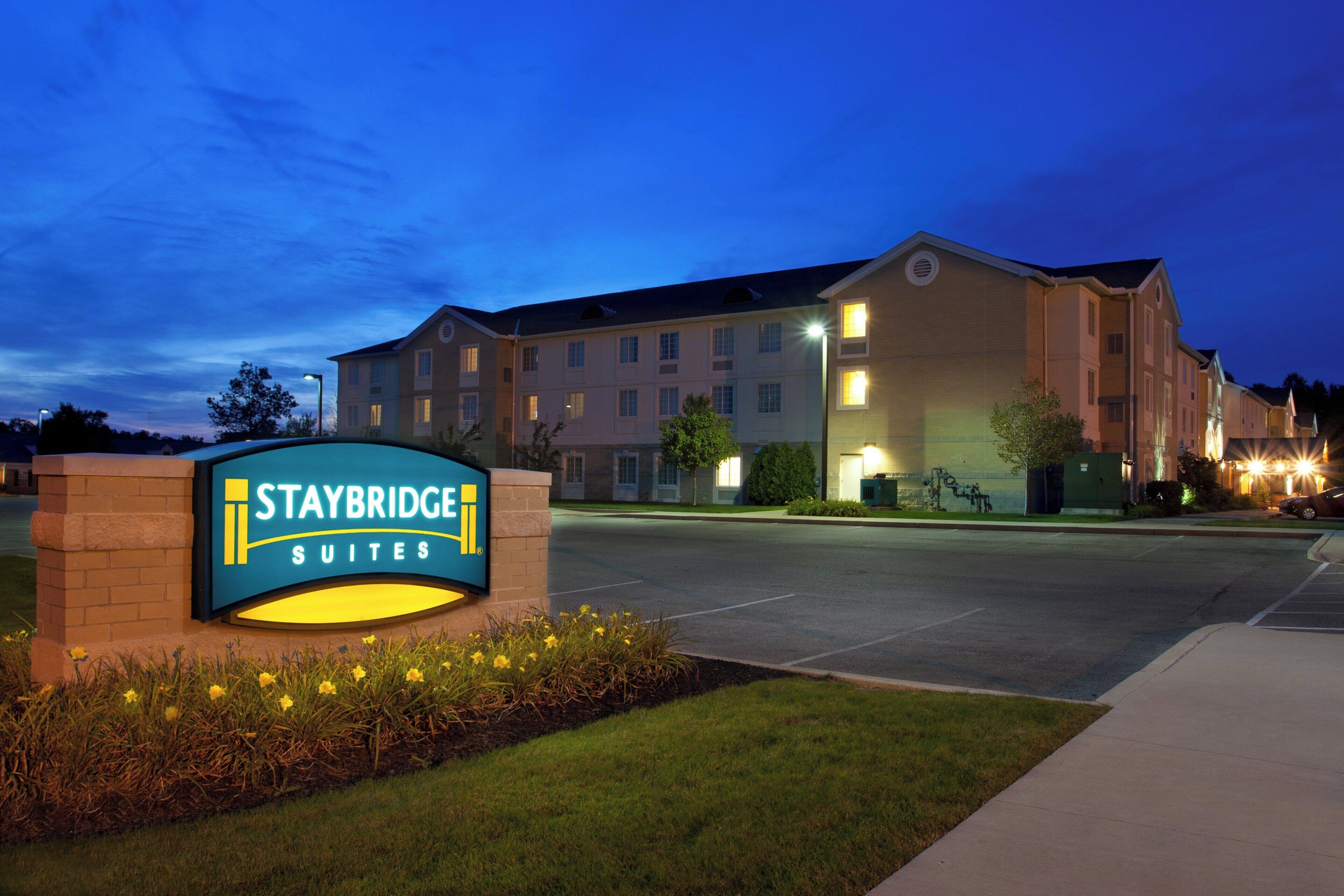 A Staybridge Suites hotel sign with a well-lit entrance and a parking lot.