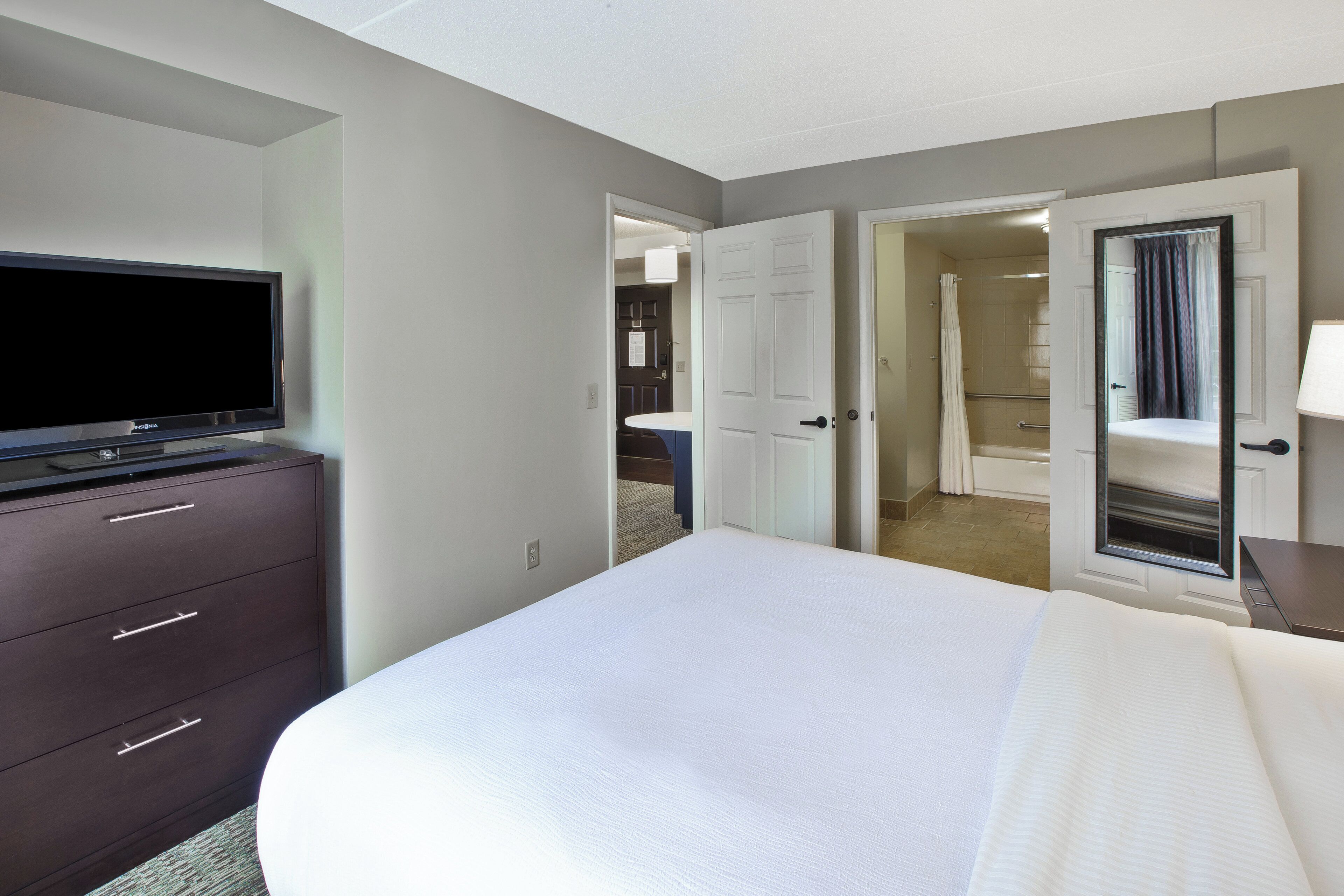 Habitación de hotel con cama, televisor, cómoda y baño visible a través de una puerta abierta.