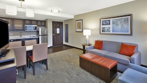 Une chambre d’hôtel moderne dotée d’un coin repas, d’une kitchenette et d’un espace salon avec un canapé et un pouf.