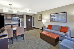 Quarto de hotel moderno com área de refeições, cozinha compacta e sala de estar com sofá e banquinho.