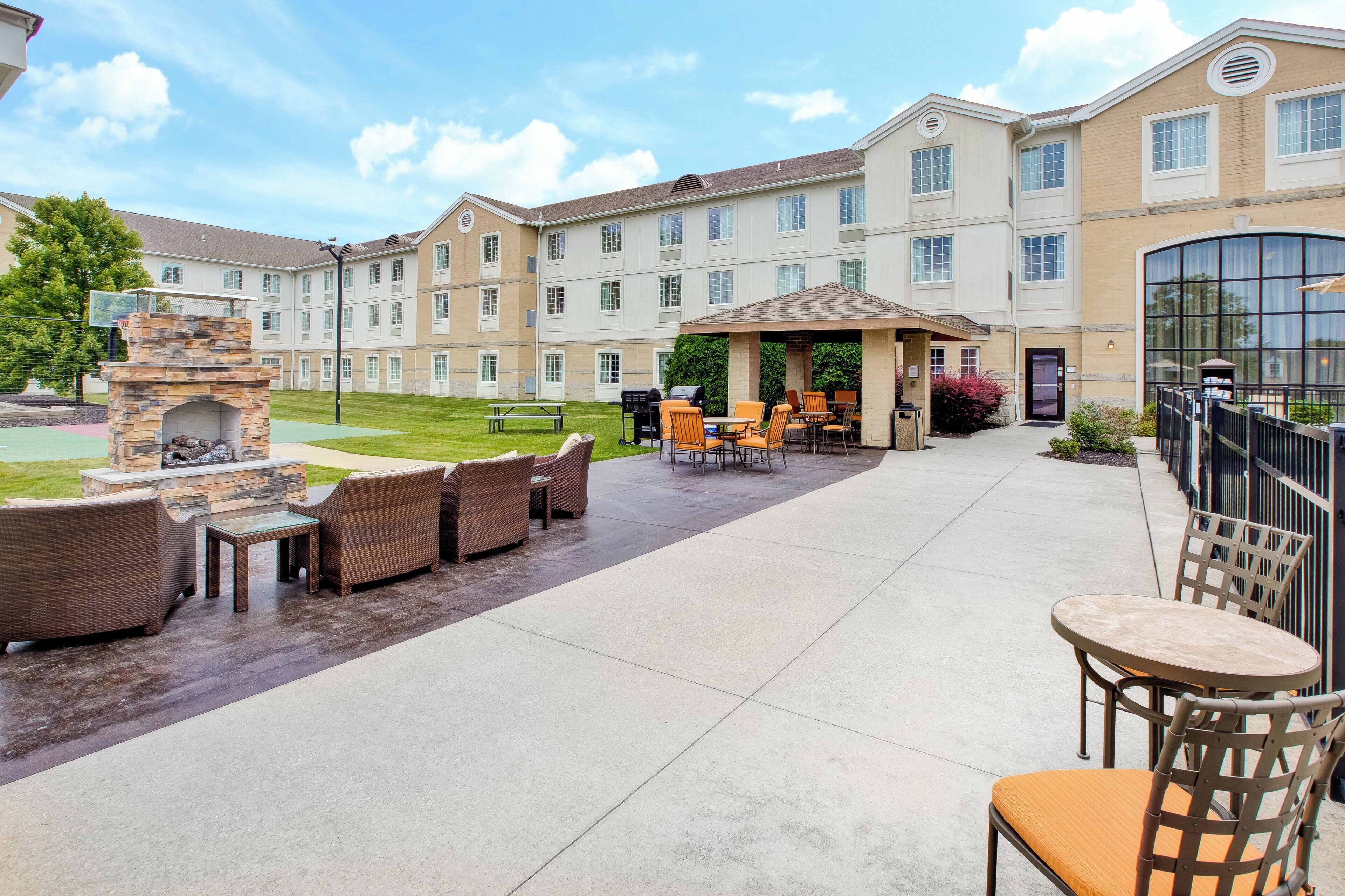 A courtyard with outdoor seating, a stone fireplace, and a building with multiple windows.