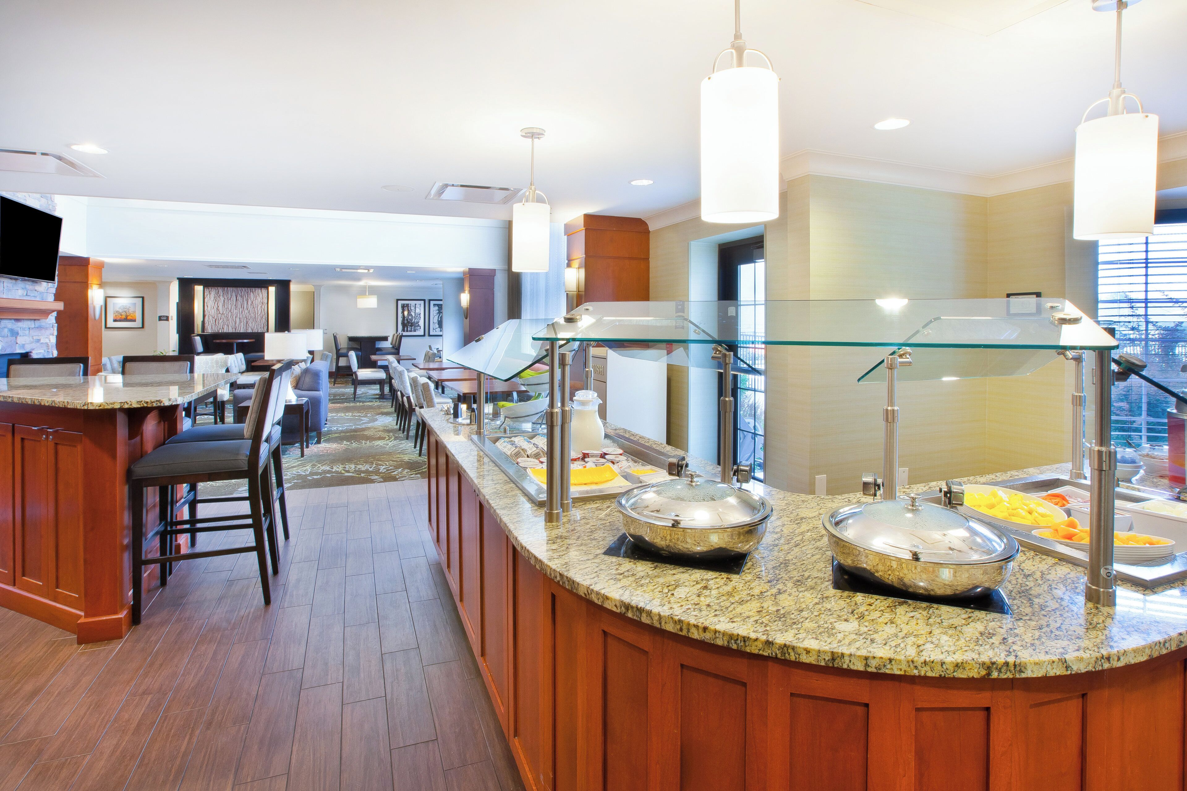 Un espace pour le petit-déjeuner à l’hôtel, avec un buffet, des tables et des chaises, et un écran de télévision.
