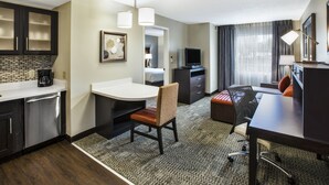 Une chambre d’hôtel équipée d’une kitchenette, d’un coin repas avec une table et des chaises, d’un lit, d’une télévision et d’un bureau avec une chaise.