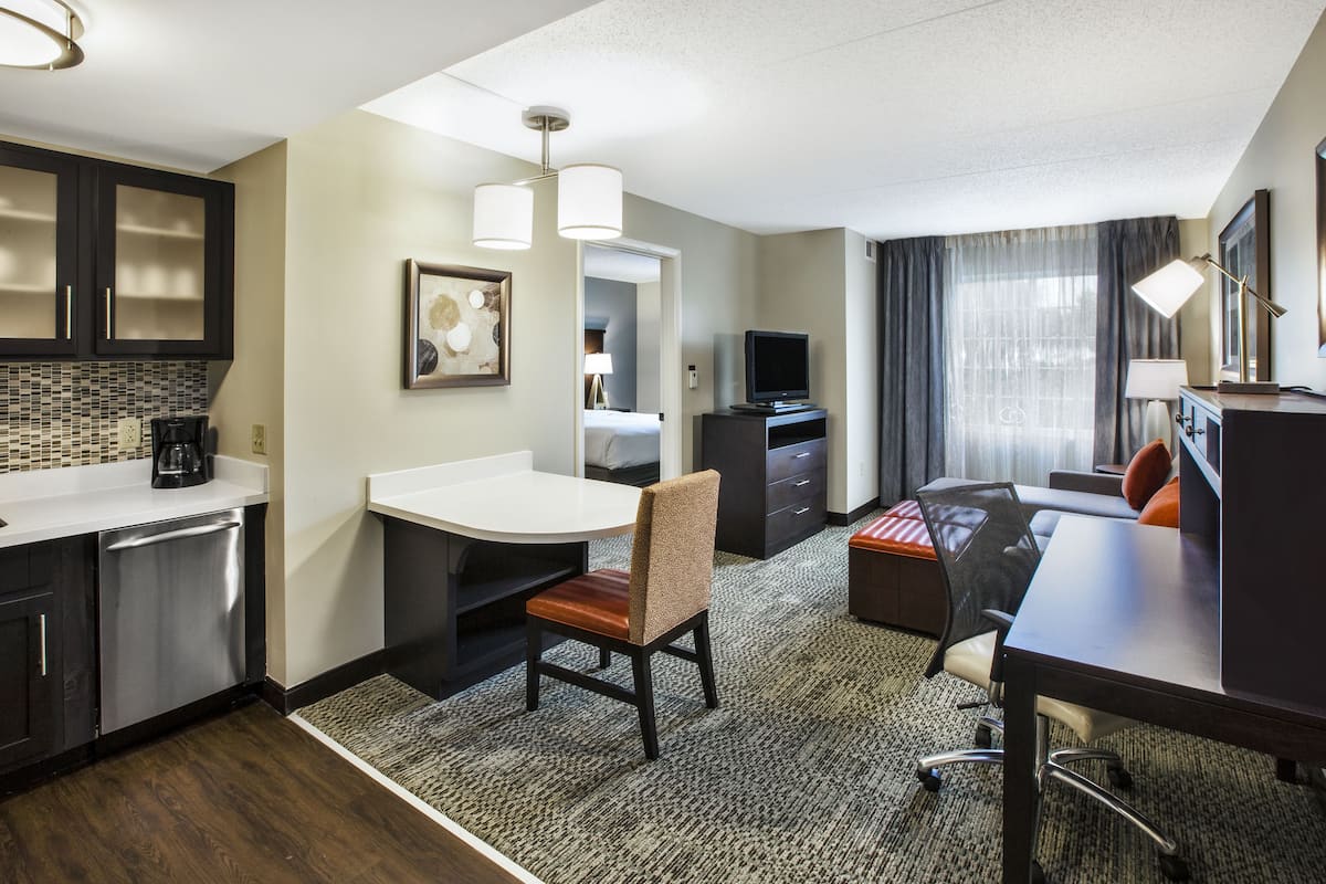 Habitación de hotel con kitchenette, zona de comedor con mesa y sillas, cama, televisión y escritorio con silla.