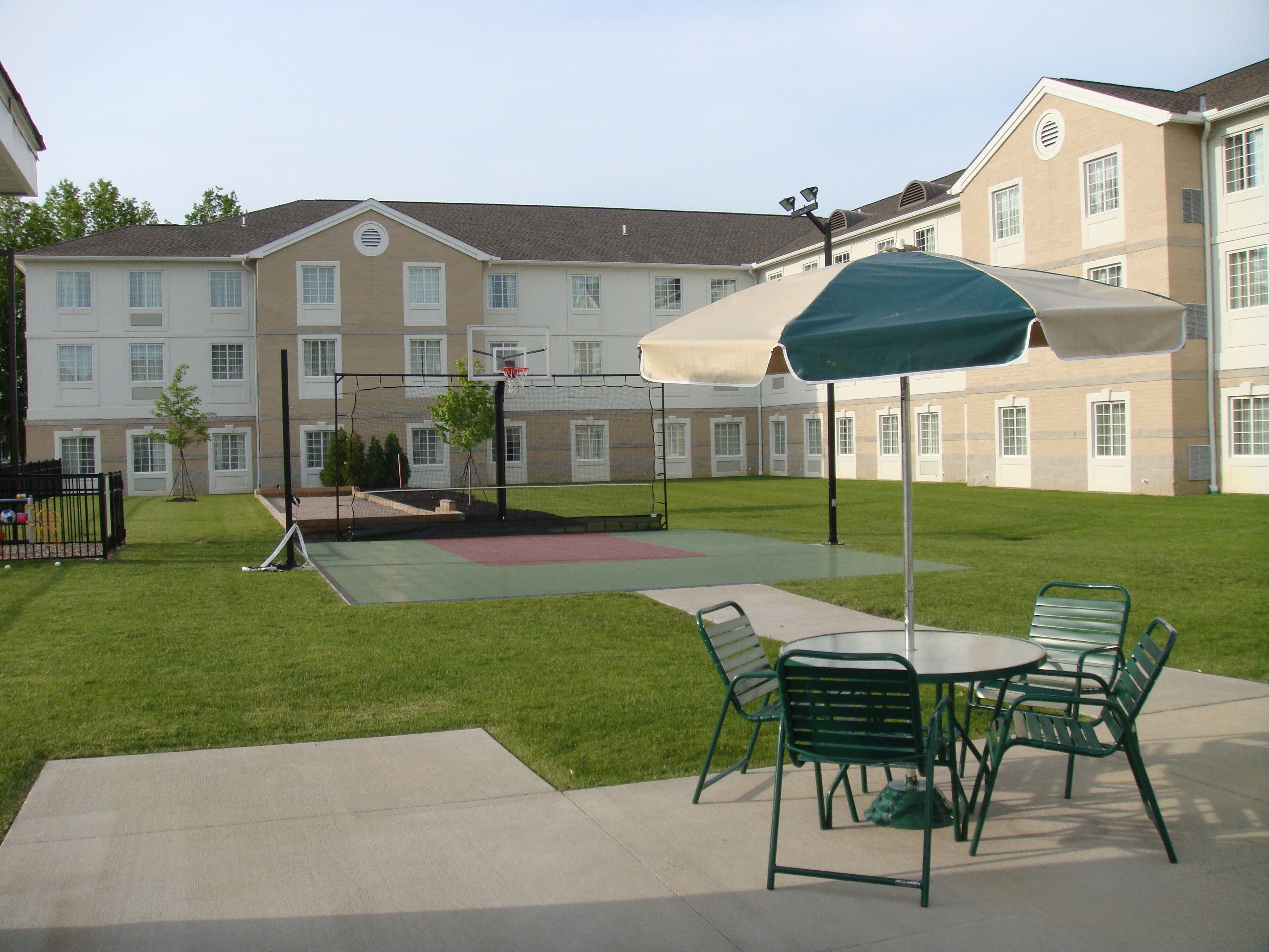 Un patio con cancha de baloncesto, mobiliario exterior y un edificio al fondo.
