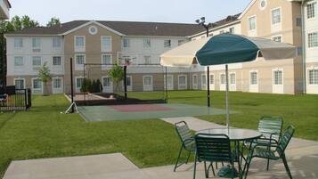 Un patio con cancha de baloncesto, mobiliario exterior y un edificio al fondo.