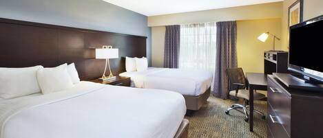 A hotel room with two beds, a desk, a TV, and a window with curtains.