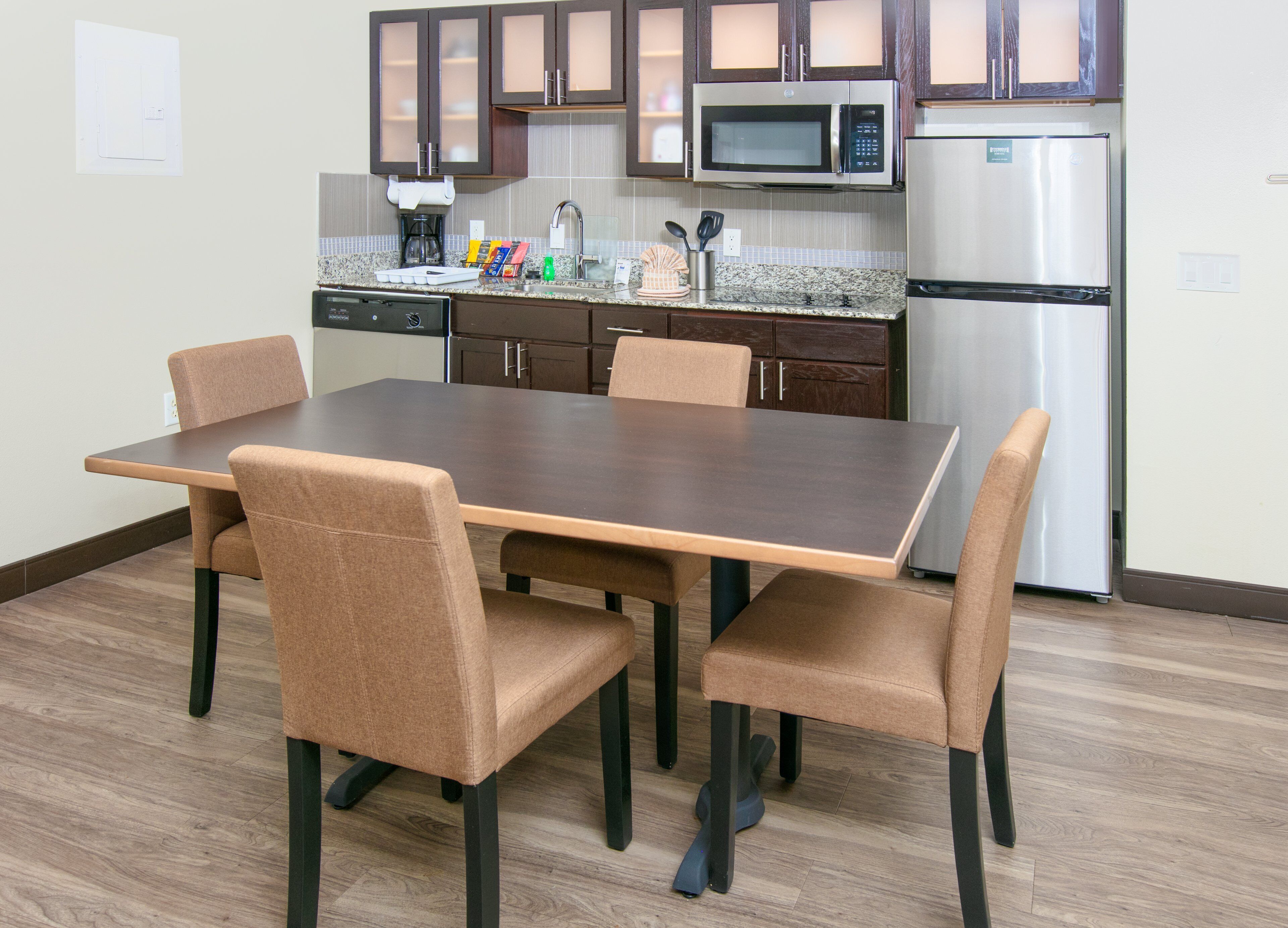 A modern kitchen with a dining table and chairs, a microwave, a refrigerator, and a dishwasher.