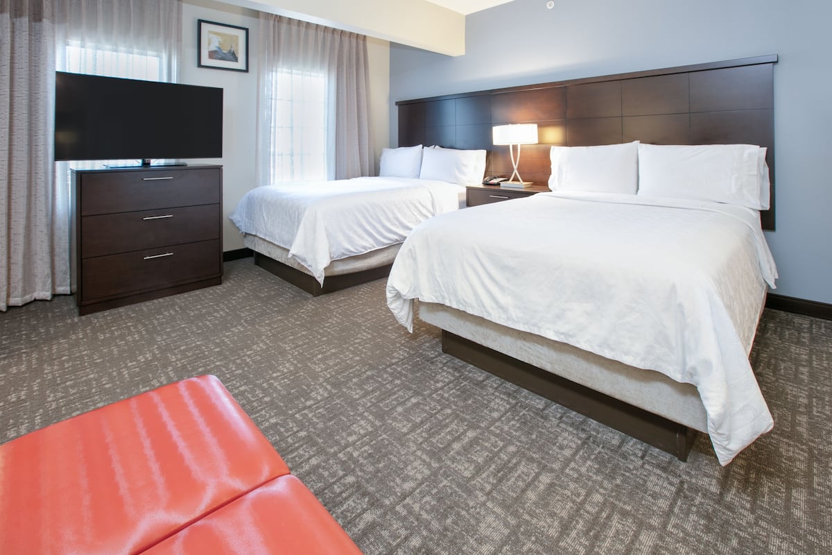 A hotel room with two beds, a TV, a desk, and a red ottoman.