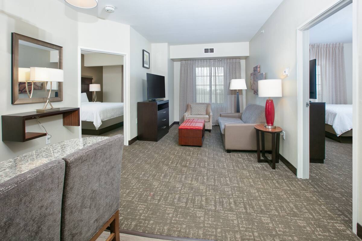 A hotel room with a bed, a sofa, a desk with a computer, a TV, and a mirror.