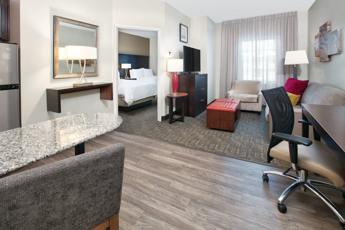 A hotel room with a bed, a desk, a chair, a sofa, a TV, and a mirror.
