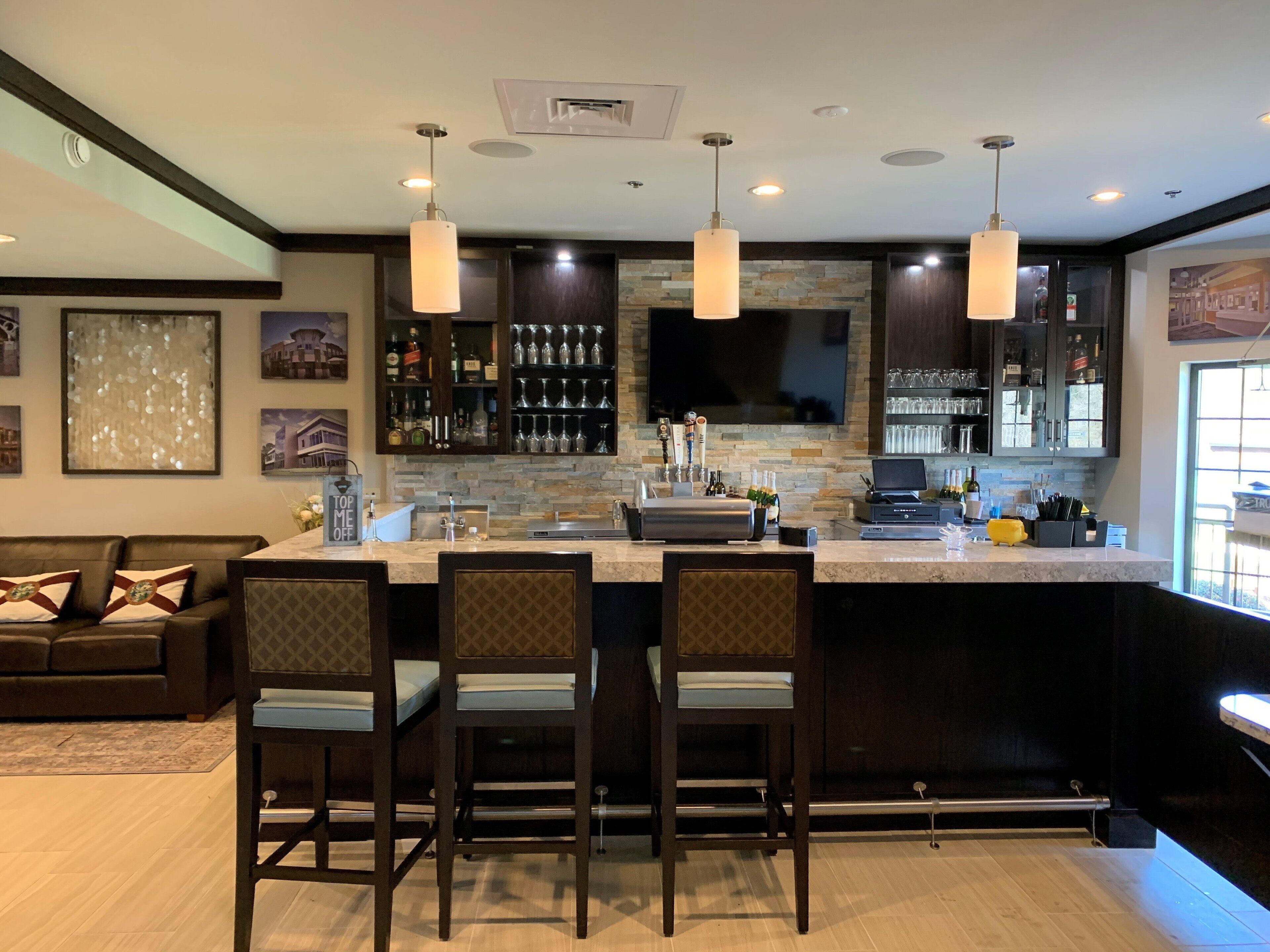 Una cocina moderna con barra, destacando un salpicadero de piedra, muebles oscuros e iluminación colgante.