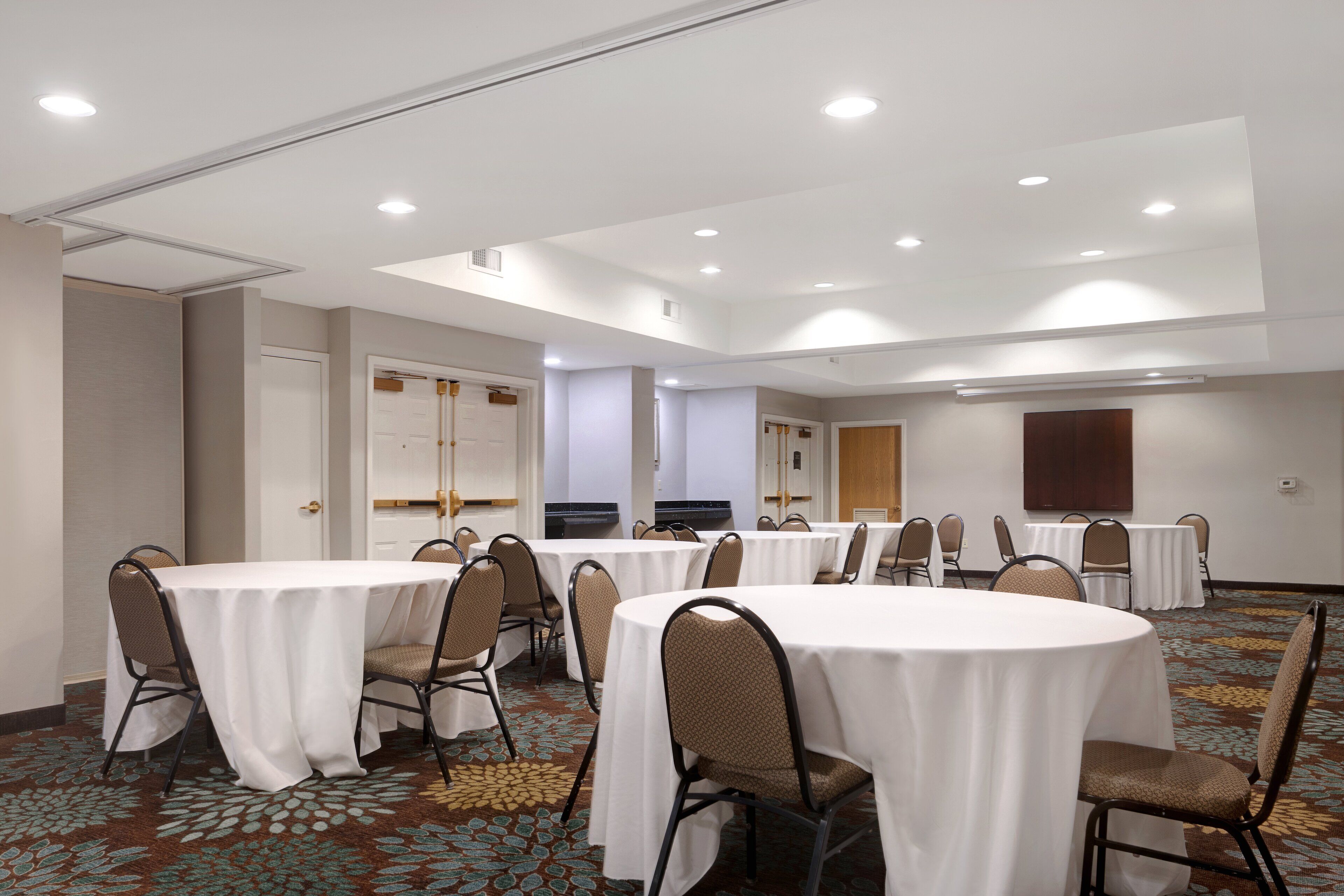 Une salle de conférence dotée de plusieurs tables rondes et de chaises, de murs blancs et d’un éclairage encastré au plafond.