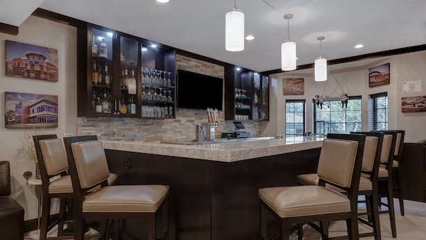 A bar area with a stone countertop, dark wooden cabinets, and bar stools. - Staybridge Suites Tallahassee by IHG (Tallahassee)