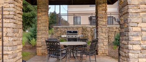 An outdoor patio with stone pillars, a round table, and metal chairs.
