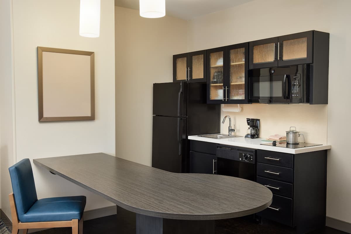 Una cocina moderna con encimera oscura, armarios negros y un lavabo blanco.