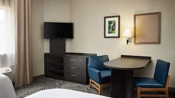 A hotel room with a bed, a desk with two chairs, a flat-screen TV, a dresser, a lamp, and a framed picture on the wall.