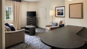Una habitación de hotel con un sofá, una mesa redonda, un televisor, una lámpara y un cuadro en la pared.