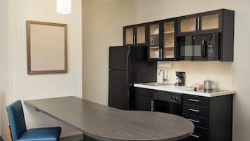 A modern kitchen with black cabinets, a stainless steel refrigerator, a microwave, and a coffee maker.