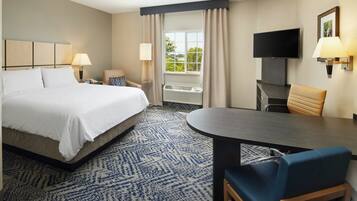 A hotel room with a bed, two bedside lamps, a television, a desk with a chair, and a large window with curtains.