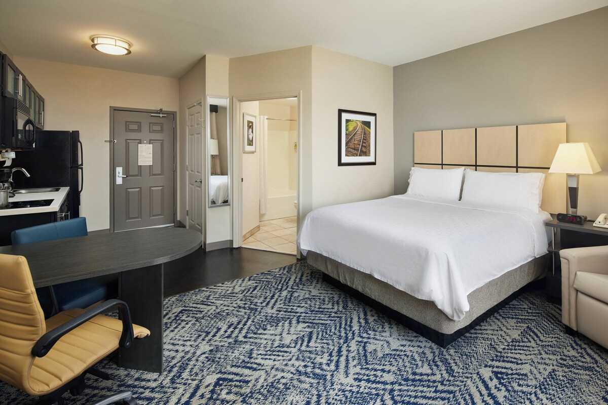 Quarto de hotel com cama, escrivaninha, cadeira e porta do banheiro.
