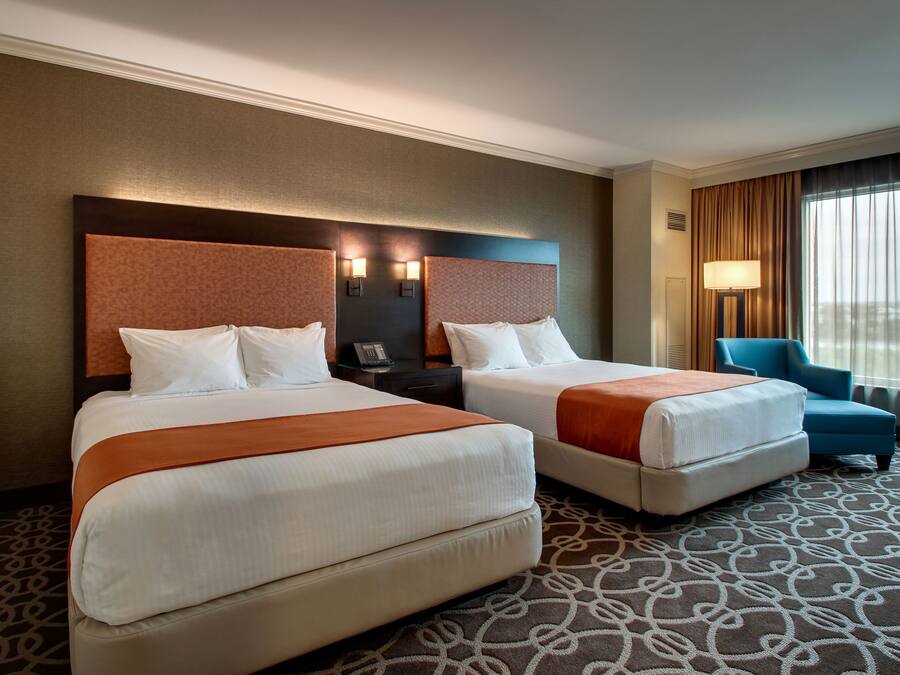 A hotel room with two beds, a desk, a chair, and a large window with curtains.