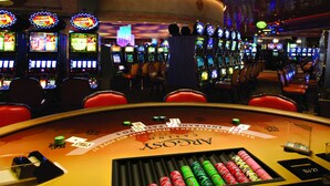 A casino gaming area with multiple slot machines, a blackjack table, and red chairs. - Argosy Casino & Hotel (Riverside)