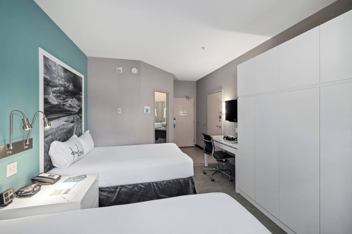 Une chambre d’hôtel avec deux lits, un bureau, une chaise, un miroir et une grande fenêtre.